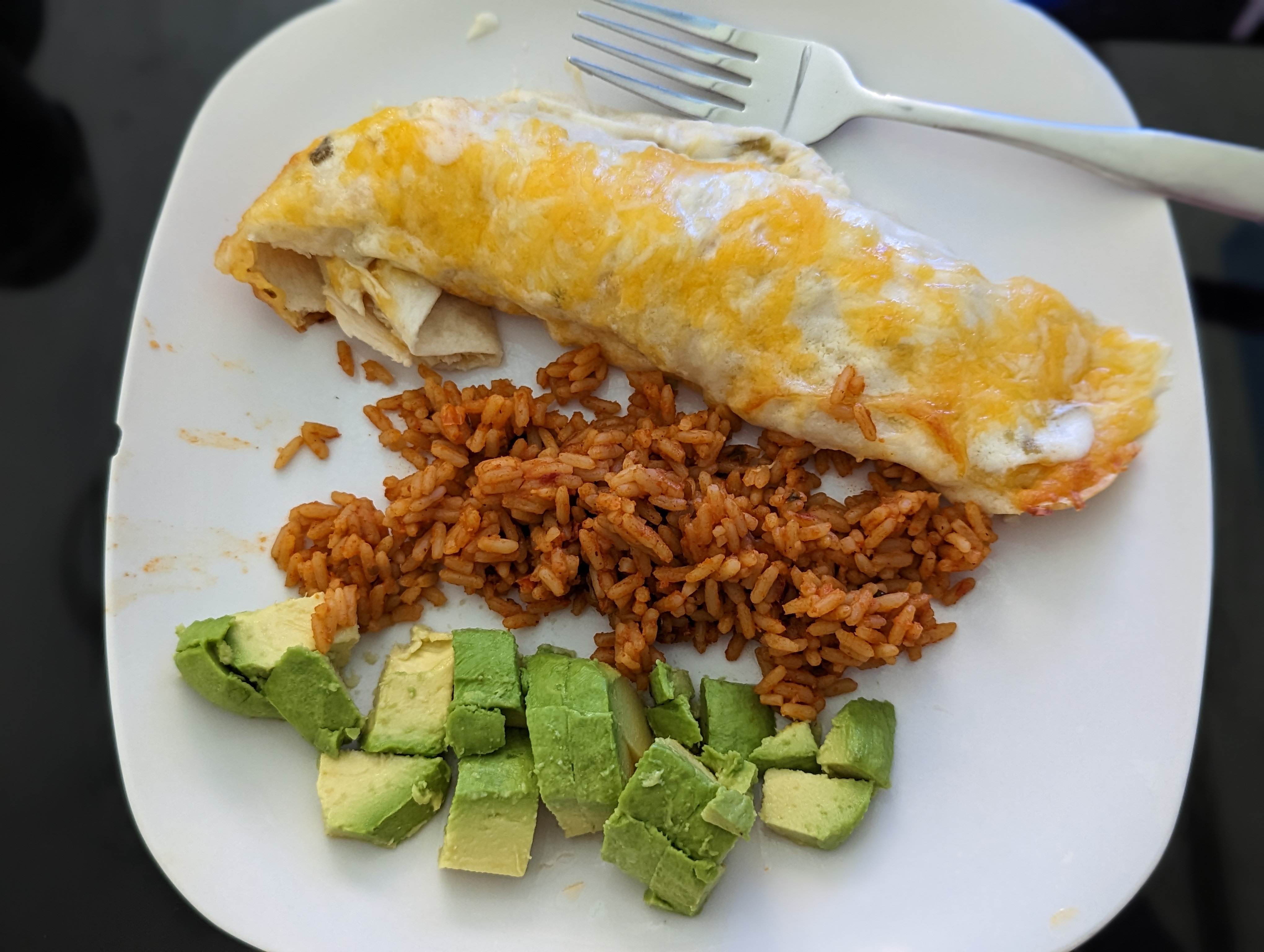 Chicken enchilada with melted mexican cheese and white sauce with sides of orange brown Spanish rice and diced avocado. 
            Image taken by Taylor Bisset